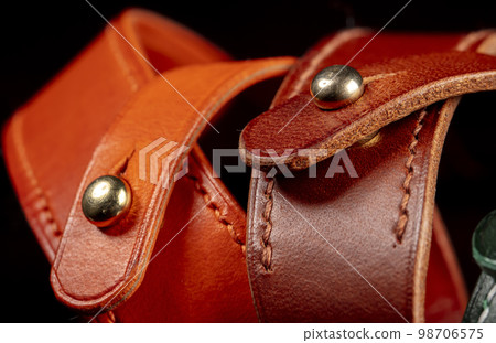 Part of a leather product or belt with a metal rivet on a black background. 98706575