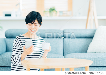 一個在客廳裡操作智能手機的女人。 98707736