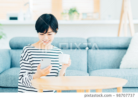 一個在客廳裡操作智能手機的女人。 一個在客廳裡操作智能手機的女人。 98707737