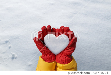 Female hand in red glove holds snow heart on snow background 98710221