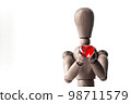 A red heart-shaped bead held by a wooden drawing doll with both hands 98711579