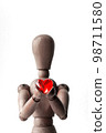 A red heart-shaped bead held by a wooden drawing doll with both hands 98711580