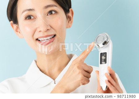 A young woman wearing a nurse uniform and explaining a facial massager Beauty image 98711980