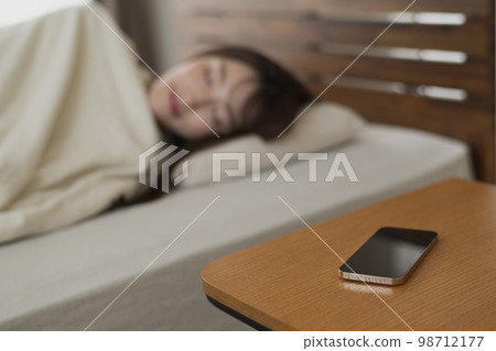 A woman sleeping with her smartphone on the side table 98712177