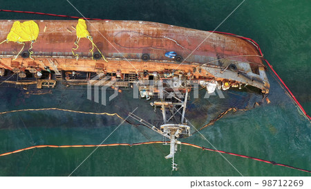 Aerial top view from drone of overturned broken rusty oil tanker ship in the shallow water. Drowned ship after the wreck. 98712269