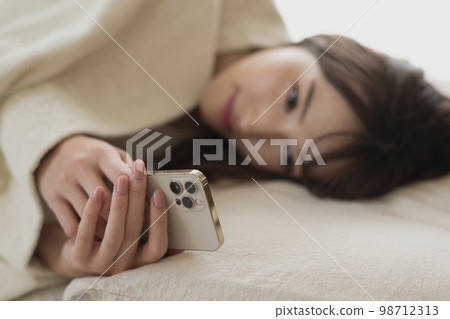一個女人在床上/臥室裡操作智能手機 98712313