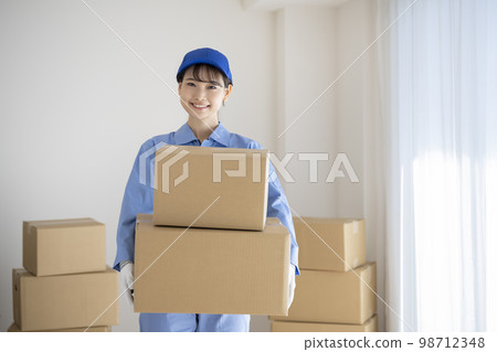 A young woman in work clothes holding a cardboard box image of a moving company 98712348