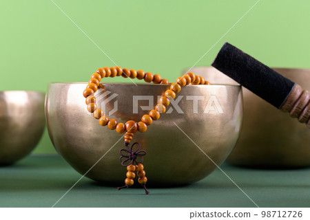 Tibetan singing bowl with stick, mala beads strands used during mantra meditations on green background 98712726