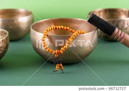 Tibetan singing bowl with stick, mala beads strands used during mantra meditations on green background 98712727