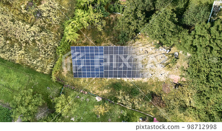 Aerial view of solar module fading away and shifting into metal supporting structure. Transition between solar panel and metal poles in grassy field with green trees. Before and after concept. 98712998