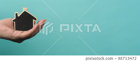 Small wood house in hands represent concepts such as home care family love real estate housing shelter insurance and mortgage. Hands holding small model house isolated on blue green studio background. 98713472