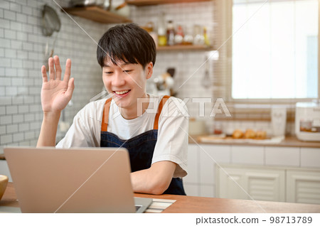 Happy Asian man in apron using laptop, having an online video call through laptop in the kitchen 98713789