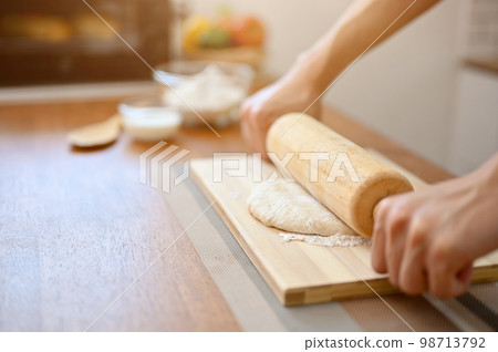 close-up image of a male baker kneading dough with a rolling pin on kitchen table 98713792