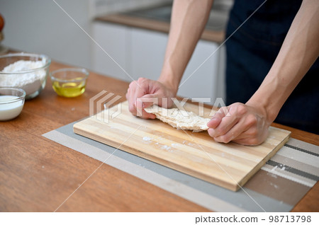 Close-up hand image of a male baker kneading raw dough, making homemade pastry at home. Close-up hand image of a male baker kneading raw dough, making homemade pastry at home. 98713798