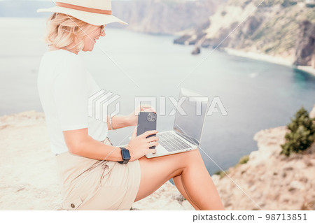 Digital nomad, Business woman working on laptop by the sea. Pretty lady typing on computer by the sea at sunset, makes a business transaction online from a distance. Freelance, remote work on vacation 98713851