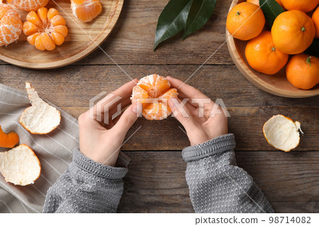 Woman holding peeled ripe tangerine at wooden table, top view 98714082