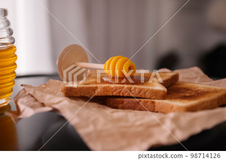 Delicious honey and toasts on parchment, closeup Delicious honey and toasts on parchment, closeup 98714126
