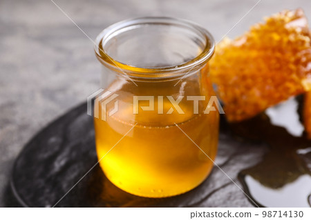 Tasty aromatic honey and combs on grey table, closeup Tasty aromatic honey and combs on grey table, closeup 98714130