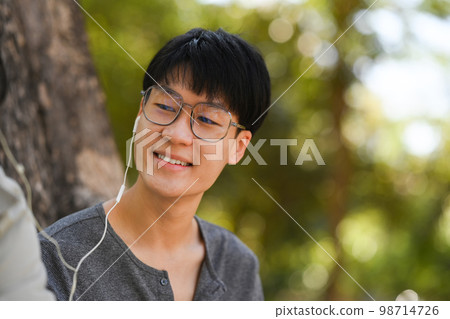 Image of young couple reading a book and listening to music in earphones while relaxing at public park together 98714726