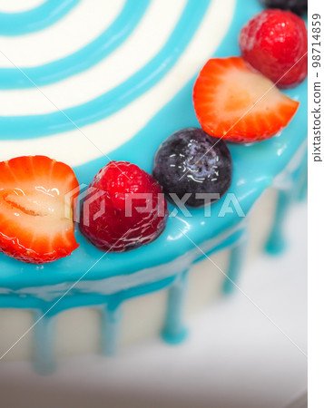 hand pastry chef designer topping a frosted white cake with pastel light blue drip filling bag 98714859