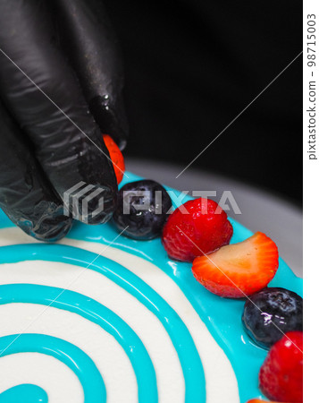 hand pastry chef designer topping a frosted white cake with pastel light blue drip filling bag 98715003