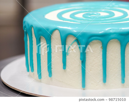 hand pastry chef designer topping a frosted white cake with pastel light blue drip filling bag 98715010