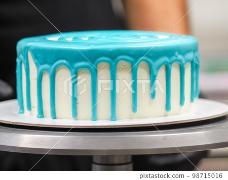 hand pastry chef designer topping a frosted white cake with pastel light blue drip filling bag hand pastry chef designer topping a frosted white cake with pastel light blue drip filling bag 98715016