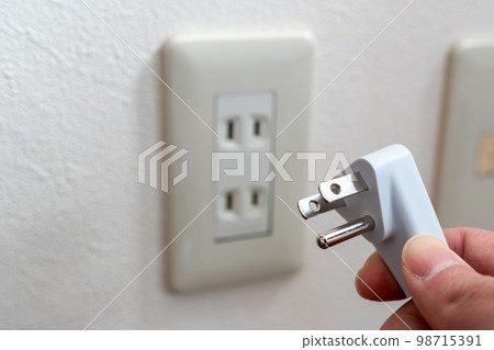 A Japanese wall socket without earth post. 3 pins power plug holding by hand.  98715391