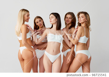 Support of friends. Protection of women. Group portrait of beautiful young women posing in underwear over grey studio background. Concept of natural beauty, body care Support of friends. Protection of women. Group portrait of beautiful young women posing in underwear over grey studio background. Concept of natural beauty, body care 98715541