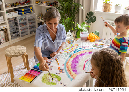 Happy young grandmother draw art picture playing grandson and granddaughter enjoy family weekend Happy young grandmother draw art picture playing grandson and granddaughter enjoy family weekend 98715964