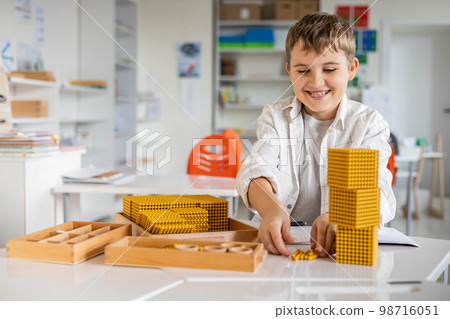 Smiling male kid with Montessori math golden bank material beads alternative counting development 98716051