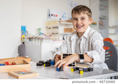 Happy male kid assembling Montessori material trinomial cube at school classroom desk Happy male kid assembling Montessori material trinomial cube at school classroom desk 98716060