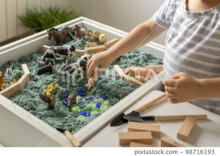 Cute baby boy playing sensory box kinetic sand table with farm animals Cute baby boy playing sensory box kinetic sand table with farm animals 98716193