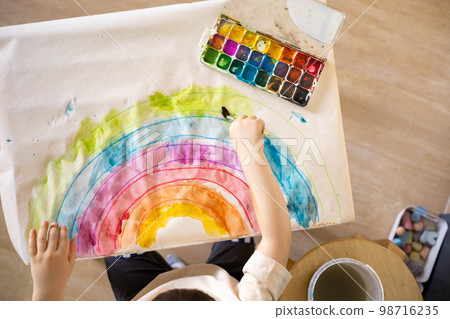 Confident cute male kid art drawing multicolored rainbow arch use paints and brush on table Confident cute male kid art drawing multicolored rainbow arch use paints and brush on table 98716235