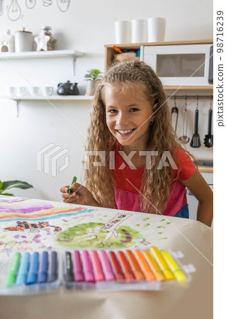 Laughing blonde curly little girl drawing paper art picture chalks sitting on near childish hovel 98716239