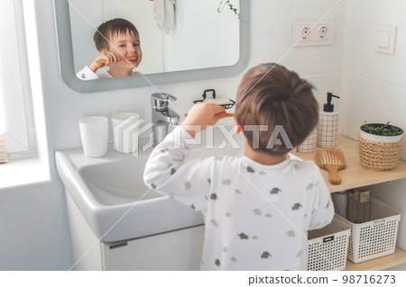 Cute male kid in pajamas cleaning teeth with eco friendly toothbrush comfortable minimalist bathroom Cute male kid in pajamas cleaning teeth with eco friendly toothbrush comfortable minimalist bathroom 98716273