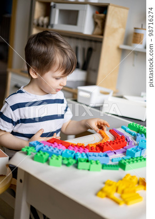 Khabarovsk, Russia, May 11, 2022. Smiling baby boy playing Lego multicolored details draw rainbow Khabarovsk, Russia, May 11, 2022. Smiling baby boy playing Lego multicolored details draw rainbow 98716274