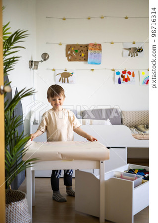 Smiling baby boy playing at cozy childish playroom interior with paper sheet rainbow arch drawing Smiling baby boy playing at cozy childish playroom interior with paper sheet rainbow arch drawing 98716314