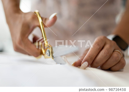 Closeup hands of female professional seamstress cutting textile use scissors making sewing sample Closeup hands of female professional seamstress cutting textile use scissors making sewing sample 98716438