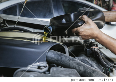 Car mechanic replacing and pouring fresh oil into engine at maintenance repair service station, Car mechanic replacing and pouring fresh oil into engine at maintenance repair service station, 98716574