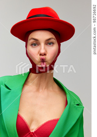 Studio Shot Of Emotive Young Stylish Girl Wearing Winter Coat And Red Heels  Doing Strange Poses On Floor Isolated Over Grey Background. Concept Of Weird  People, Art, Fashion. Looks Funny Stock Photo