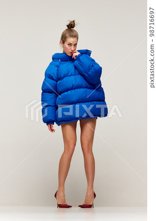 Studio shot of emotive young stylish girl wearing winter coat and red heels doing strange poses on floor isolated over grey background. Concept of weird people, art, fashion Studio shot of emotive young stylish girl wearing winter coat and red heels doing strange poses on floor isolated over grey background. Concept of weird people, art, fashion 98716697