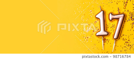 Gold candles in the form of number seventeen on yellow background with confetti. 17 years celebration. Gold candles in the form of number seventeen on yellow background with confetti. 17 years celebration. 98716784
