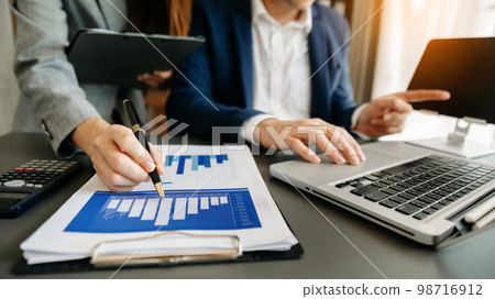 Business coworkers colleagues working together, have a discussion and using tablet and laptop computer at office with financial document on desk. Business coworkers colleagues working together, have a discussion and using tablet and laptop computer at office with financial document on desk. 98716912