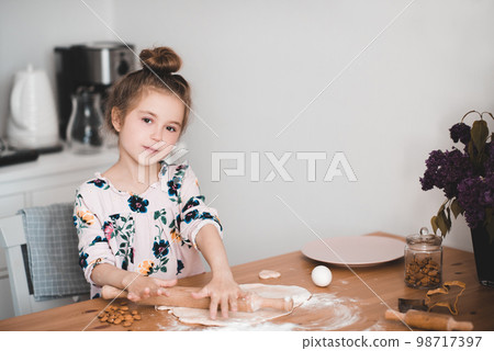 Smiling kid girl 4-5 year old making cake in kitchen. Cooking child in room. Childhood. Looking at camera. Smiling kid girl 4-5 year old making cake in kitchen. Cooking child in room. Childhood. Looking at camera. 98717397