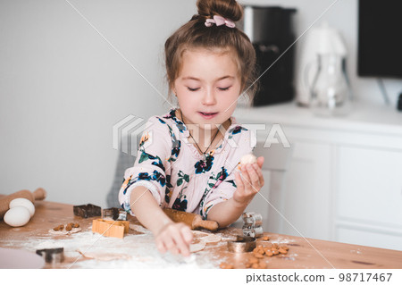 Beautiful baby girl 4-5 year old making Christmas gingerbread in kitchen closeup. Winter season. Childhood. 98717467