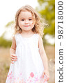 Cute happy baby girl 2-3 year old walking in meadow on green background. Smiling child. Childhood. Looking at camera. 98718000