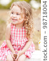 Funny baby girl 2-3 year old  sitting in meadow outdoors. Laughing child. Looking away. Childhood. 98718004
