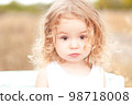 Cute baby girl with blonde curly hair outdoors. Little girl 2-3 year old. 98718008