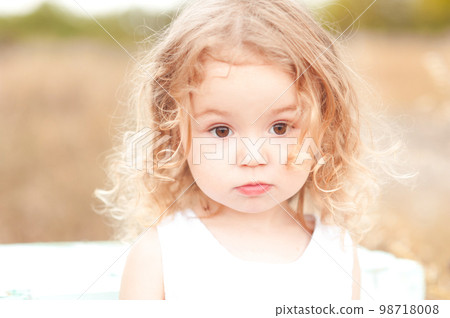 Cute baby girl with blonde curly hair outdoors. Little girl 2-3 year old. 98718008